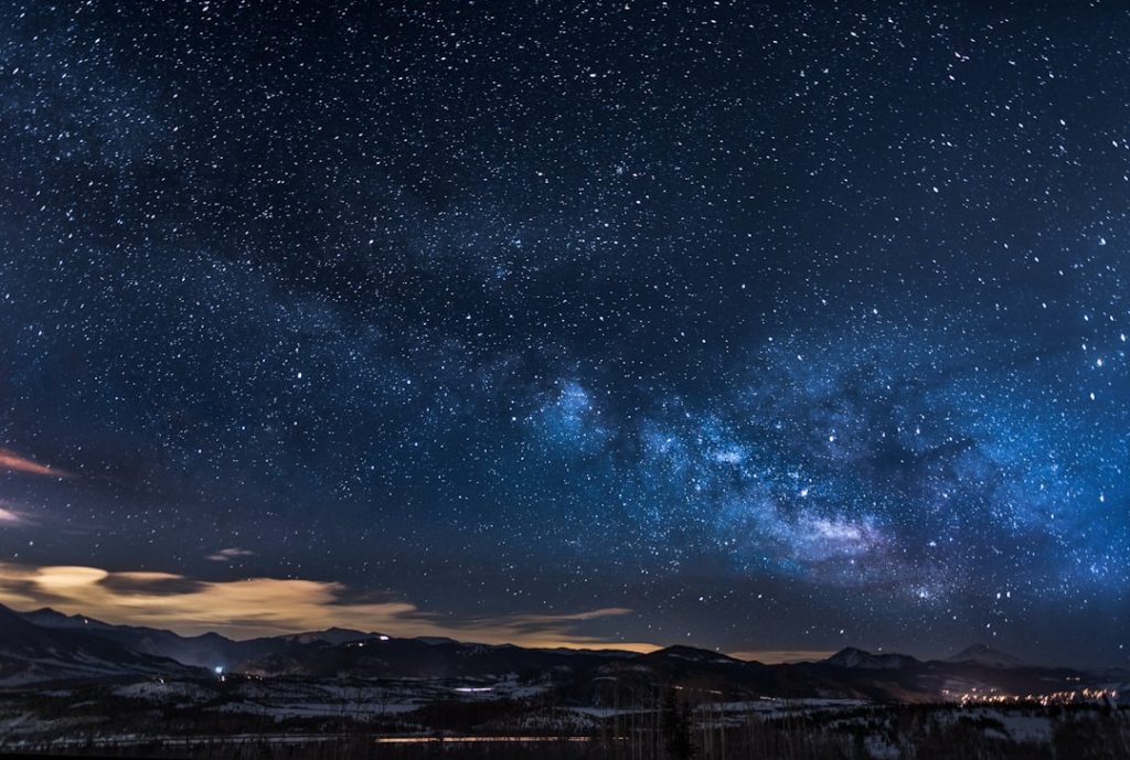 A clear night sky filled with stars and a faint zodiac wheel overlay, evoking astrology and celestial themes